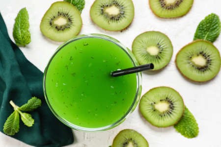 Glass of healthy green juice and fresh kiwi slices on light backgroundの写真素材