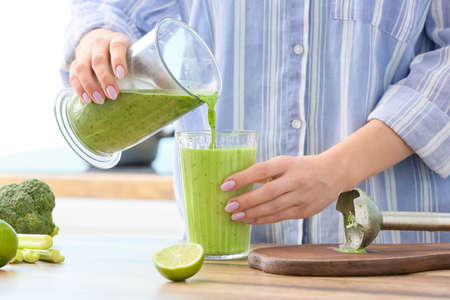 Woman pouring green juice into glass at table, closeupの写真素材