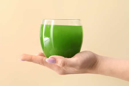 Woman holding glass of green juice on beige backgroundの写真素材