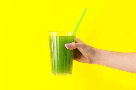 Woman holding glass of green juice on yellow backgroundの写真素材