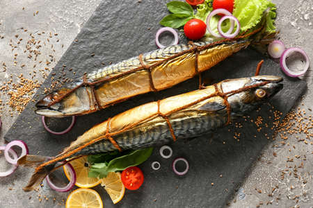 Board with smoked mackerel fishes on gray background