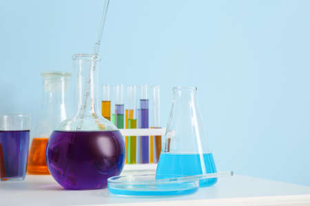 Different laboratory glassware with samples on table near blue wall
