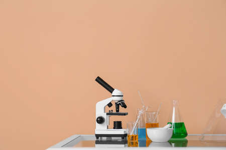 Modern microscope and laboratory glassware with liquid on table near beige wall