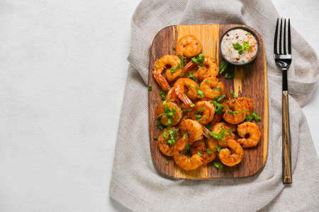 Wooden board of tasty shrimp tails with sauce on white backgroundの写真素材
