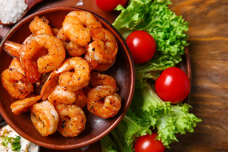 Plate of tasty shrimp tails and tomatoes on tableの写真素材