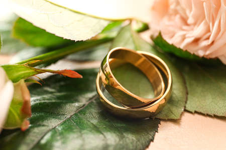 Golden wedding rings and green leaves on beige background, closeup
