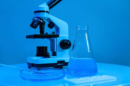 Different laboratory glassware with samples and microscope on table near blue wallの写真素材