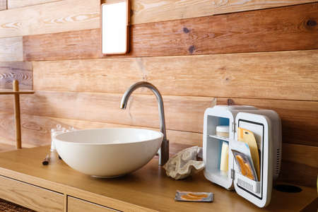Open cosmetic refrigerator and sink on table near wooden wallの写真素材