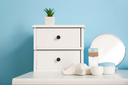 Drawers with flowerpot and bath accessories on shelf near blue wall