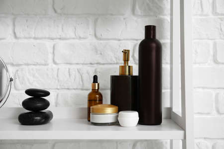 Bottles of cosmetic products and spa stones on shelf near white brick wallの写真素材
