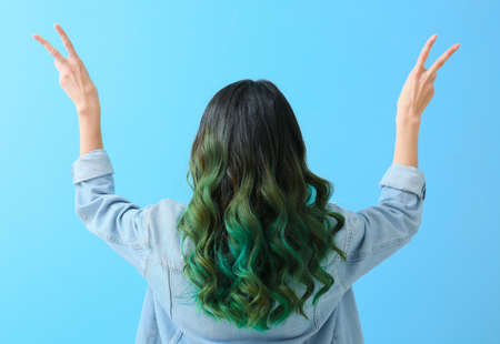 Beautiful young woman with unusual green hair showing victory gesture on color backgroundの写真素材