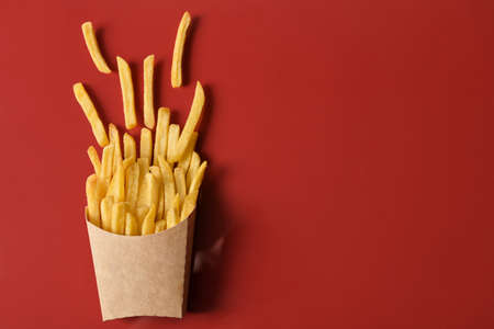 Paper box with tasty french fries on red background