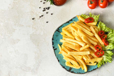 Plate with tasty french fries on light background