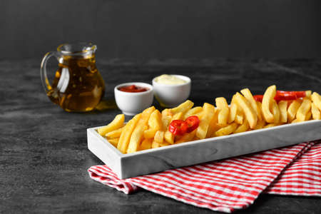 Board with tasty french fries on black background, closeup