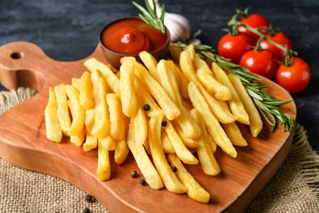 Wooden board with tasty french fries on black backgroundの写真素材