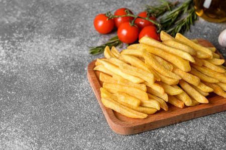 Wooden board with tasty french fries on gray background, closeup