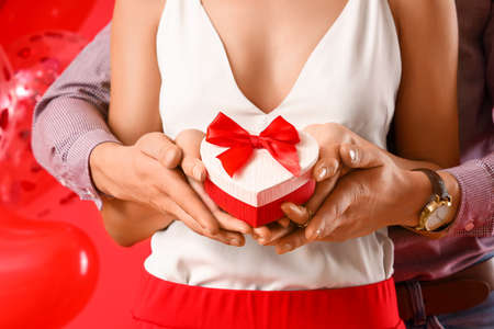 Happy young couple with gift on color background, closeup. Valentine's Day celebrationの写真素材