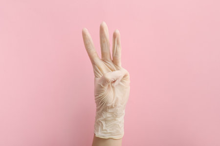 Woman in medical glove showing three fingers on pink backgroundの写真素材