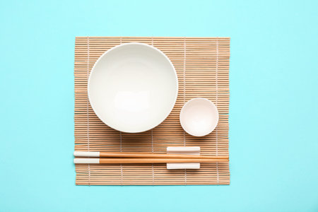 Bamboo mat with Chinese bowls and chopsticks on color backgroundの写真素材