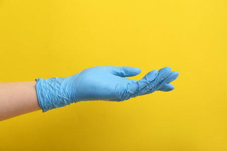 Woman in blue medical glove on yellow backgroundの写真素材