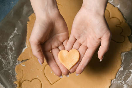 Woman holding uncooked heart shaped cookie at table. valentine's day celebration