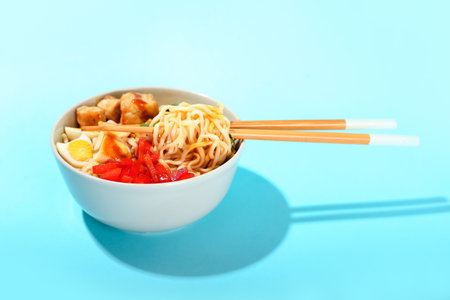 Bowl of tasty noodles with chicken on blue backgroundの写真素材