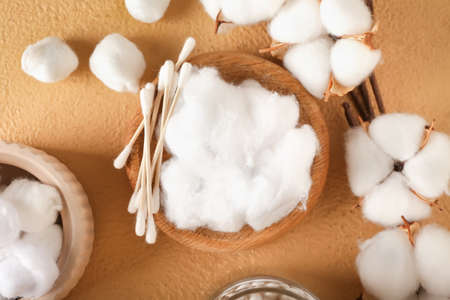 Bowl of cotton wool, swabs and flowers on color background, closeup