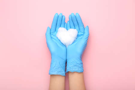 Female hands in rubber gloves and cotton wool heart on pink background, closeup
