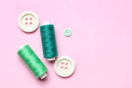 Sewing threads with buttons on pink background