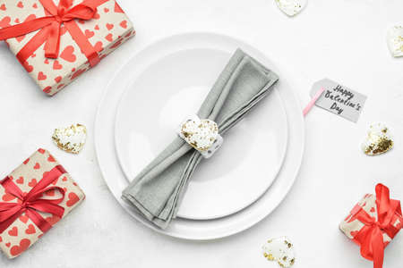 Beautiful table setting with gift boxes and tag with text HAPPY VALENTINE'S DAY on white background