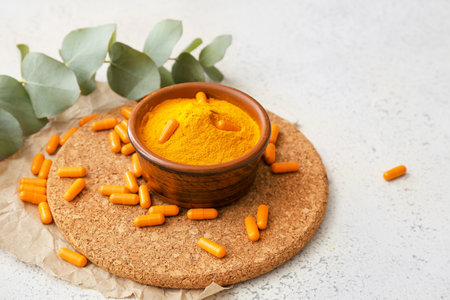 Bowl with turmeric powder and capsules on light backgroundの写真素材