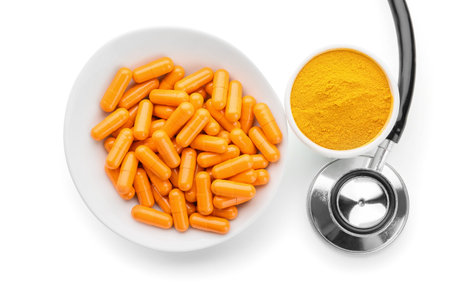 Bowl with turmeric capsules, powder and stethoscope on white backgroundの写真素材