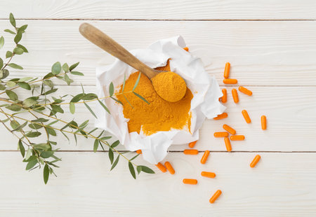 Parchment with turmeric powder and capsules on light wooden background