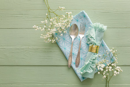 Stylish cutlery with flowers on green wooden background