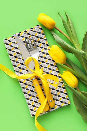 Stylish cutlery with tulip flowers on green background