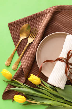 Stylish table setting with tulip flowers on green background