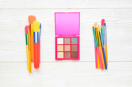 Set of makeup brushes and eye shadows on light wooden background