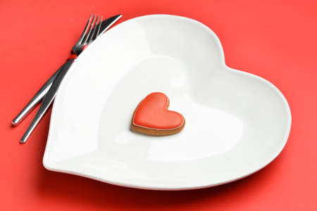 Beautiful heart-shaped plate and cutlery on red background, closeup