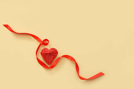 Beautiful wicker heart and red ribbon on beige background. St. Valentine's Day