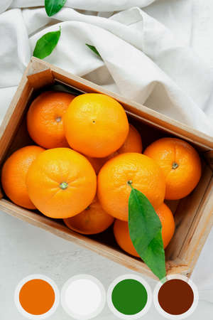 Wooden box with fresh juicy oranges on light background. Different color samples