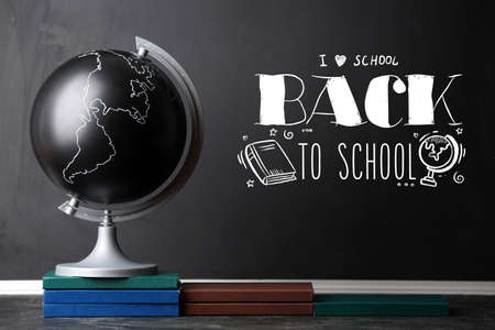 Globe and books on table near blackboard with text BACK TO SCHOOL