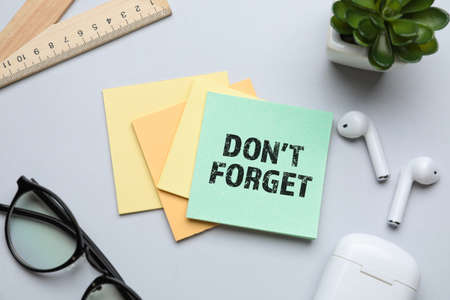 Sticky note with text DON'T FORGET, eyeglasses, earphones and ruler on light backgroundの写真素材