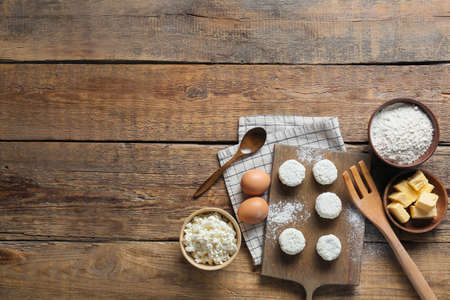 Board with uncooked cottage cheese pancakes and ingredients on wooden backgroundの写真素材