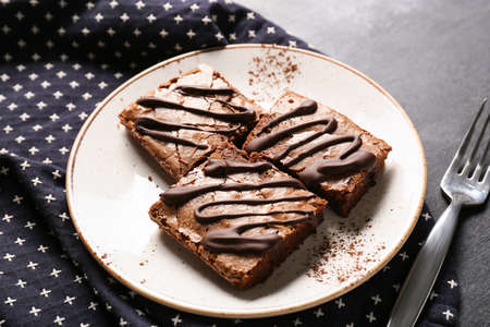 Plate with pieces of tasty chocolate brownie on black background