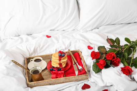 Wicker tray with delicious breakfast, bouquet of roses and gift for Valentine's Day on bedの写真素材