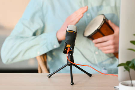 Modern microphone on table of man playing drum in room, closeup