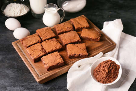 Wooden board with pieces of tasty chocolate brownie on black backgroundの写真素材