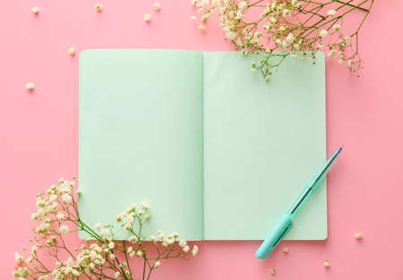 Blank notebook, pen and gypsophila flowers on pink background