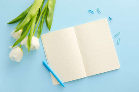 Open notebook, pen and tulips on color background