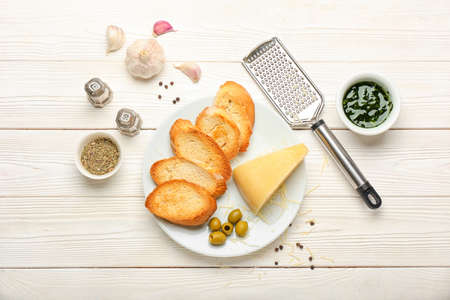 Plate of tasty croutons with cheese and grater on white wooden backgroundの写真素材